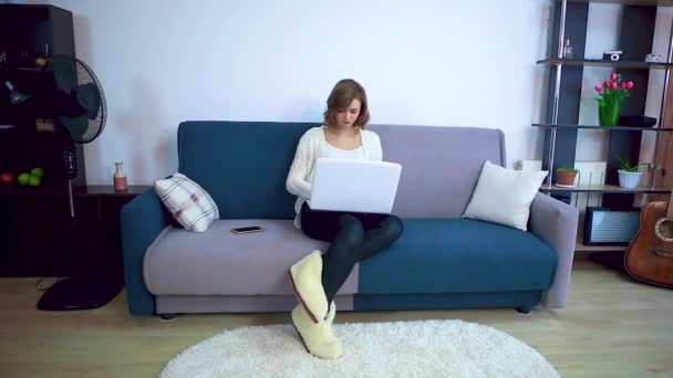 Menina trabalhando em um laptop enquanto sentado em um sofá . — Vídeo de Stock