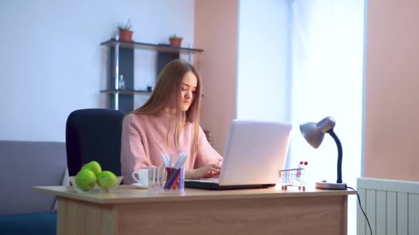 Mujer joven trabaja en un ordenador portátil en un trabajo remoto . — Vídeos de Stock