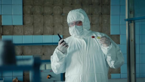 Медицинский работник в защитном костюме и очках держит рацию в руках лаборатории, говорящей о ней. . — стоковое видео