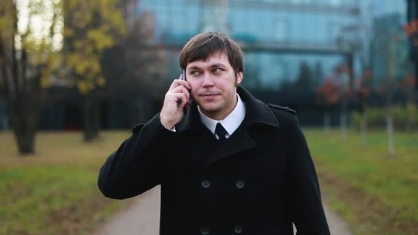 Бизнесмен, гуляющий по парку и разговаривающий по телефону . — стоковое видео