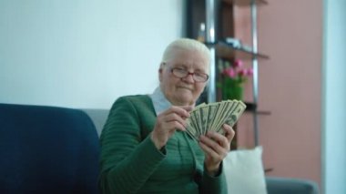 Yaşlı kadın kanepede otururken para sayıyor.