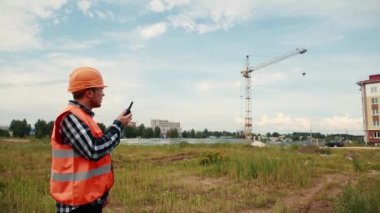 Turuncu yelekli ve miğferli bir adam, kuleye bakan bir telsize konuşur..