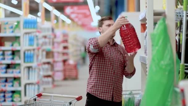 Un uomo in un negozio seleziona un contenitore di liquido nel suo carrello . — Video Stock