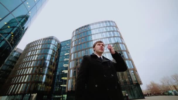 Мужчина-бизнесмен в черном пальто разговаривает по телефону на улице в бизнес-центре . — стоковое видео