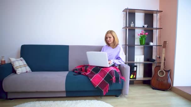 Girl on the couch wrapped in a checkered plaid communicates via video link on a laptop. — Stock Video