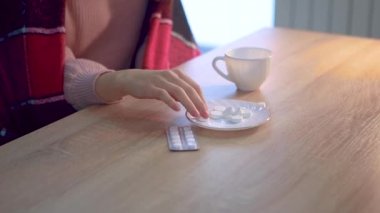 Ekoseye sarılı bir kız masaya oturur ve soğuk algınlığı için hap içer..