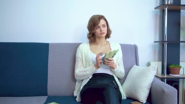 Flickan räknar pengar sittandes på soffan. — Stockvideo