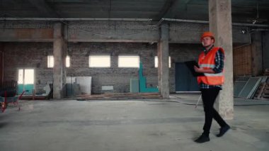 Turuncu yelek ve turuncu miğferli bir erkek müteahhit inşaat alanında veri özetliyor..
