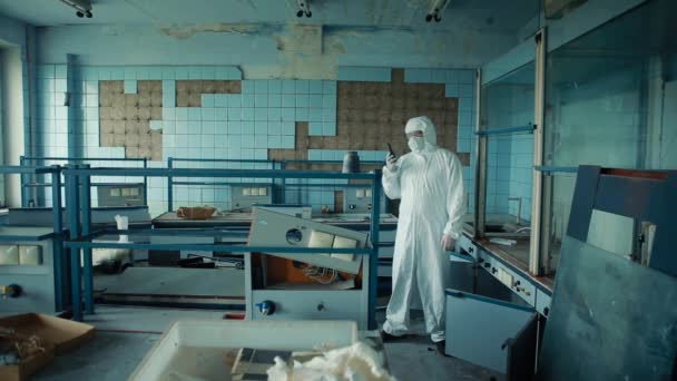 Ένας γιατρός με προστατευτική στολή και γυαλιά στέκεται σε ένα κατεστραμμένο εργαστήριο και επικοινωνεί μέσω ενός γουόκι-τόκι.. — Αρχείο Βίντεο