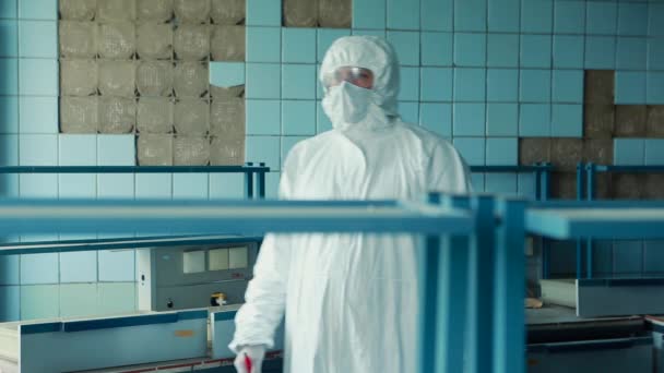 Lab technician in a protective suit and goggles approaches the table in the laboratory and begins to record data. — Stock Video