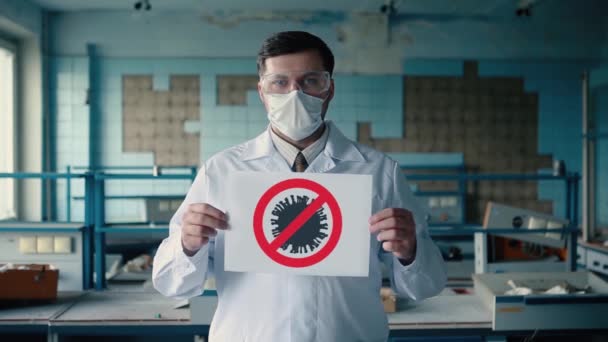 Человек в защитном костюме в маске и очках держит постер с вирусом остановки. . — стоковое видео