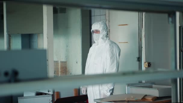 Un homme en costume de protection et lunettes est debout près de la porte du laboratoire, regardant autour de lui . — Video