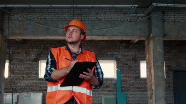 Turuncu yelek ve turuncu kask takmış bir erkek müteahhit..