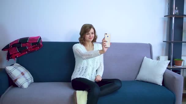 The girl sits on the couch and communicates via video. — Stock Video