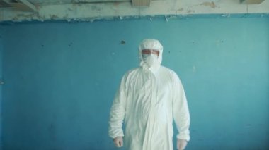 Koruyucu giysili ve gözlüklü bir adam terk edilmiş bir laboratuvarda yürüyor..