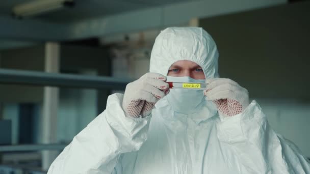 Närbild av en forskare i mask och skyddsdräkt håller och undersöker ett prov av covid-19 i ett laboratorium. — Stockvideo