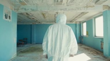 Koruyucu takım elbiseli ve gözlüklü laboratuar teknisyeni, tecrit bölgesindeki terk edilmiş bir laboratuvarda sırtüstü yürüyor..