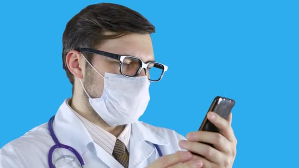Чоловік у медичній шубці та масці розмовляє по телефону через відеозв'язок . — стокове відео