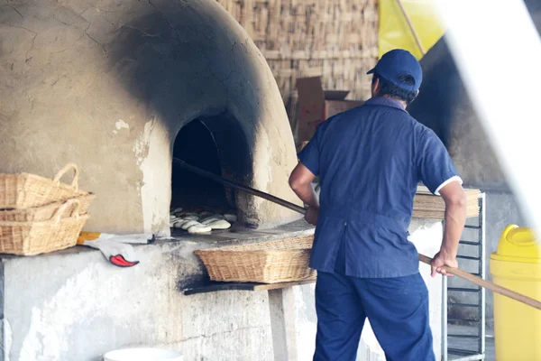 Человек печет хлеб в деревенской традиционной духовке — стоковое фото