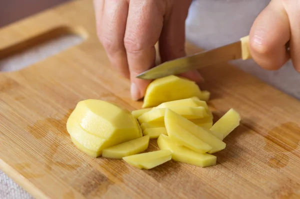 Kadın soyulmuş patates bir ahşap tahta üzerinde bir bıçakla keser