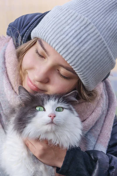 Girl with eyes closed hugs a cat and smiles