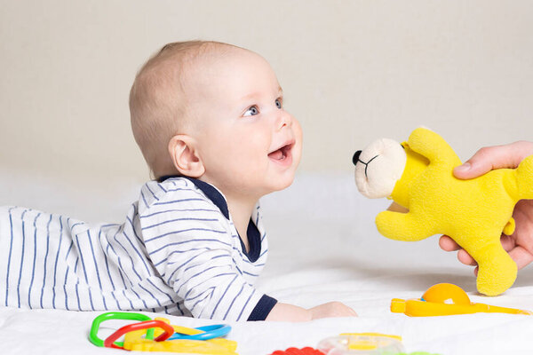 Ребенок лежит на животе, улыбается и смотрит на папу, который вручает ему игрушку