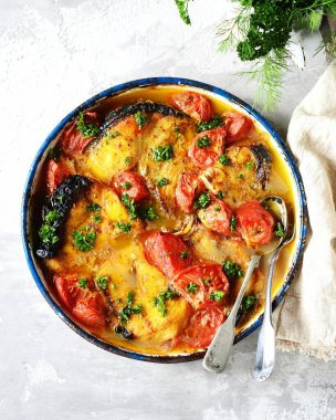 Fırınlanmış balık (köpekbalığı) domates ve baharatlarla gri arka planda pişirme kabında, durgun yaşam