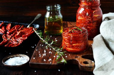 Koyu bir arka planda cam kavanozlarda ev yapımı kurutulmuş domatesler.