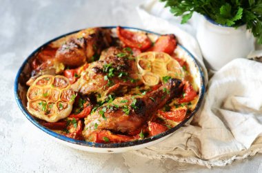 Domatesle pişirilmiş tavuk budu ve gri arka planda bir fırın kabında sarımsak