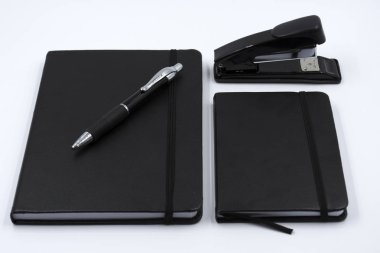 siyah deri Not defteri, kalem ve beyaz arka plan üzerinde zımba. Masaüstü Seti. Ofis masaları. İşe geri.