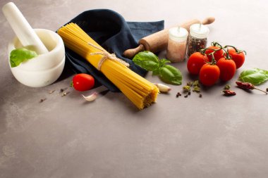 İtalyan makarnası için ham malzemeler: çiğ spagetti, taze domates, deniz tuzu, kurutulmuş biber, taze fesleğen yaprağı ve gri arka planda fotokopi alanı olan sarımsak..