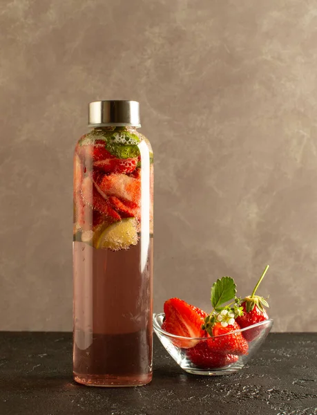 Fresh strawberry lemonade or cocktail with strawberries,lime and mint leaves in bottle with refreshing mineral water.Close up.