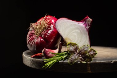 Olgun kırmızı soğan, taze biberiye, mor fesleğen, sarımsak ve kurutulmuş biber ahşap masada, siyah arka planda..