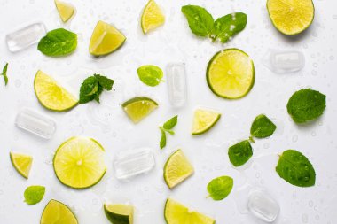 Taze limon dilimleri, nane yaprakları, buz küpleri ve su damlalarıyla beyaz gıda arka planı..