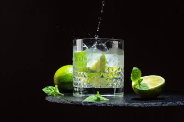 Kristal bardakta soğuk mojito kokteyli veya limonlu limonata, taş tabakta nane yaprağı ve buz küpleri..