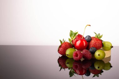 Yansımalı taze olgun meyveler: çilek, Bektaşi üzümü, kiraz ve ahududu..