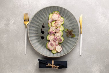 Turşulu taze salata, kırmızı soğan, susam tohumu ve gri seramik tabakta mor fesleğen yaprağı, çatal ve bıçakla. Vegan yaz salatası..