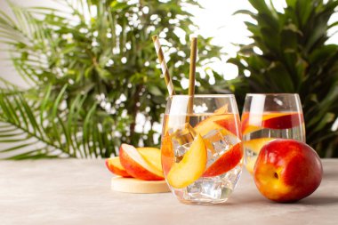 Şeftali kokteyli ya da arkaplanda taze şeftali ve tropikal bitkilerle birlikte limonata. Yaz kokteylinin ferahlatıcısını kapat..