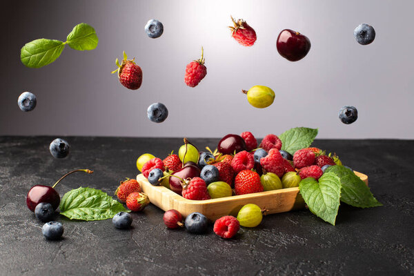 Various falling Summer Berries on the table with wooden plate with berries and fresh mint leaves.Food levitation.