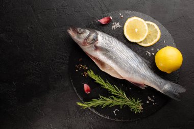 Taze biberiyeli çiğ deniz levreği ve taş plakalı siyah beton arka planda limon..