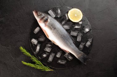 Buz küplü taze deniz levreği, biberiye, siyah arka planda limon..