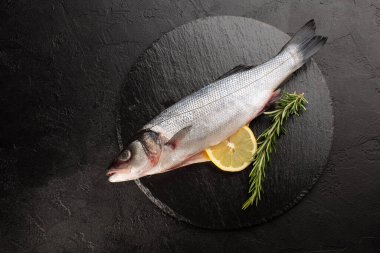 Taze biberiyeli çiğ deniz levreği ve taş plakalı siyah beton arka planda limon..