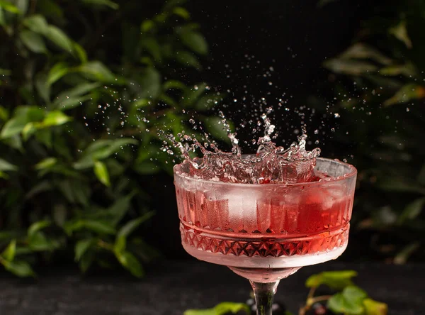 Splash di rinfrescante cocktail estivo rosa in vetro di cristallo margarita con piante tropicali sullo sfondo.. — Foto Stock