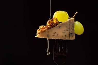 Çatala bal damlatan Gorgonzola dilimleri, siyah arka planda ceviz ve üzümler. Peynirli atıştırmalıkları kapatın..
