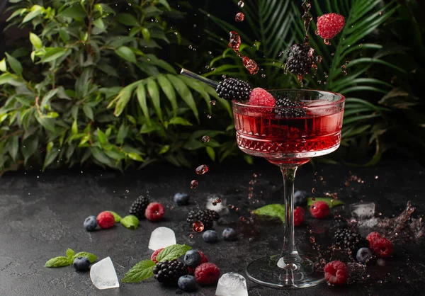 Cocktail di frutti di bosco freschi con lampone, mora, menta e ghiaccio con piante tropicali sullo sfondo. Colpo di bevanda in movimento congelato, gocce volanti e frutti di bosco. Bevanda fredda estiva e cocktail. — Foto Stock