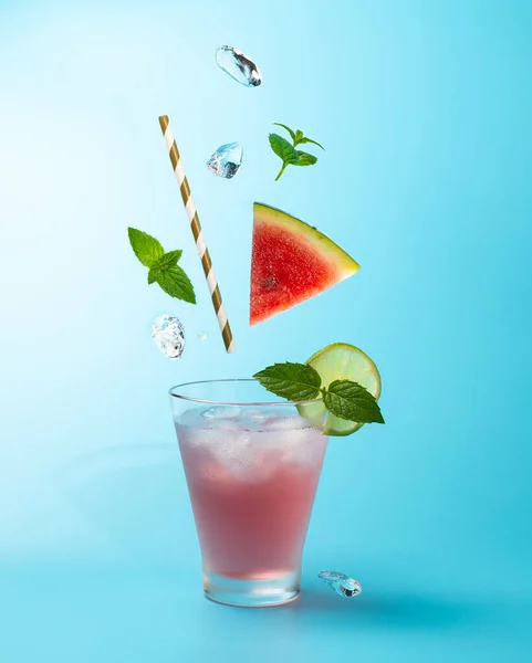 Cocktail all'anguria con cubetti di ghiaccio, vite di menta e lime su fondo azzurro.Colpo di bevanda in freeze motion, ghiaccio volante, foglie di menta e anguria.. — Foto Stock