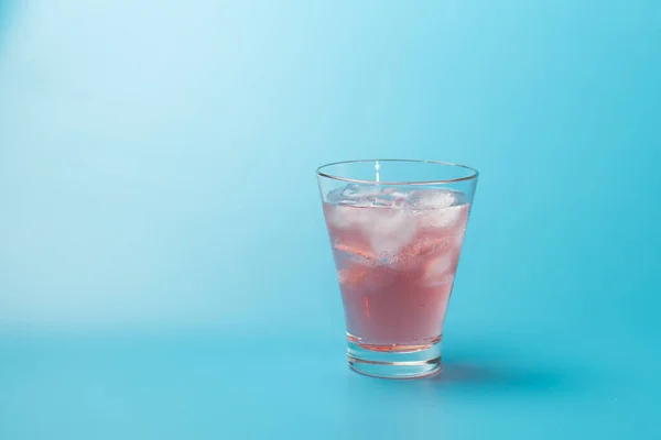 Verre de cocktail rose rafraîchissant ou thé glacé avec glaçons sur fond bleu avec espace de copie. — Photo