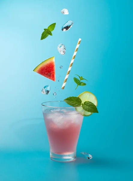 Cocktail all'anguria con cubetti di ghiaccio, vite di menta e lime su fondo azzurro.Colpo di bevanda in freeze motion, ghiaccio volante, foglie di menta e anguria.. — Foto Stock