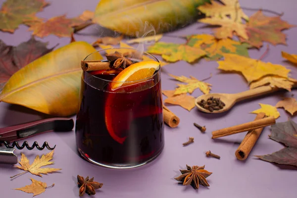 Wino musujące z cynamonem, pomarańczami, gwiazdami anyżu, jesiennymi, żółtymi liśćmi i dymem z gorącego napoju na fioletowym tle.Jesienna, przytulna martwa natura z gorącym napojem bezalkoholowym. — Zdjęcie stockowe