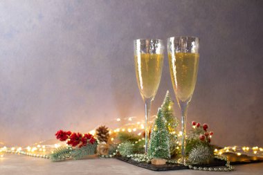 İçinde Noel ağaçları, minyatürler, köknar dalları, boncuklar, noel süslemeleri ve noel ışıkları olan iki kadeh..